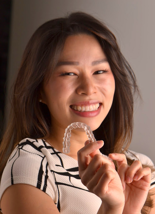 smiling woman holding Invisalign clear aligner in alexandria