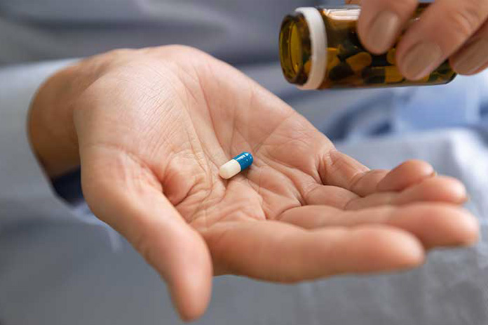 person holding a blue-white capsule from a pill bottle for dental sedation
